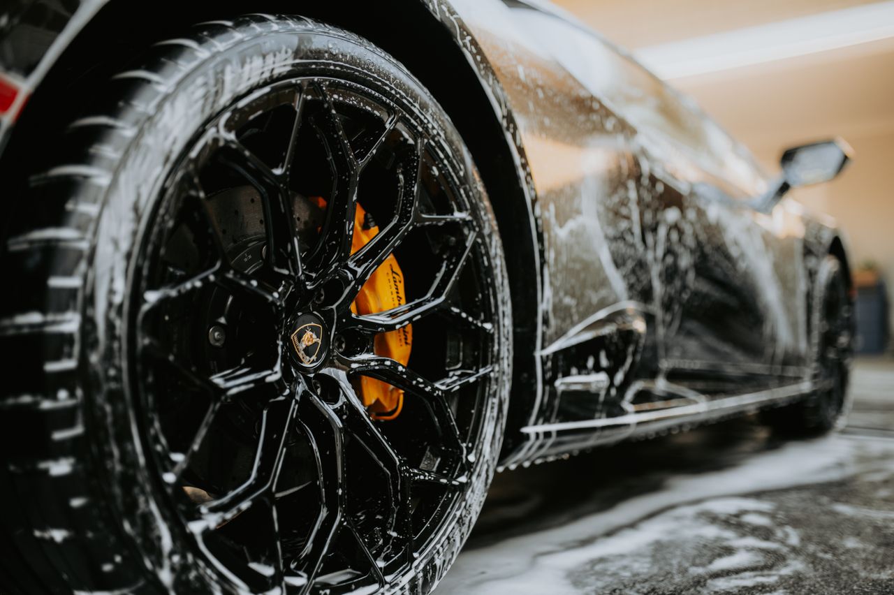 trusted-partner Detailed close-up of a luxury car wheel covered in soap suds during a professional car wash.