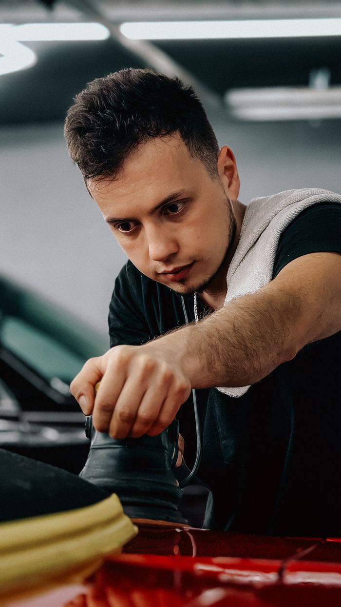 services-01 Young man working meticulously on car detailing indoors with professional equipment.