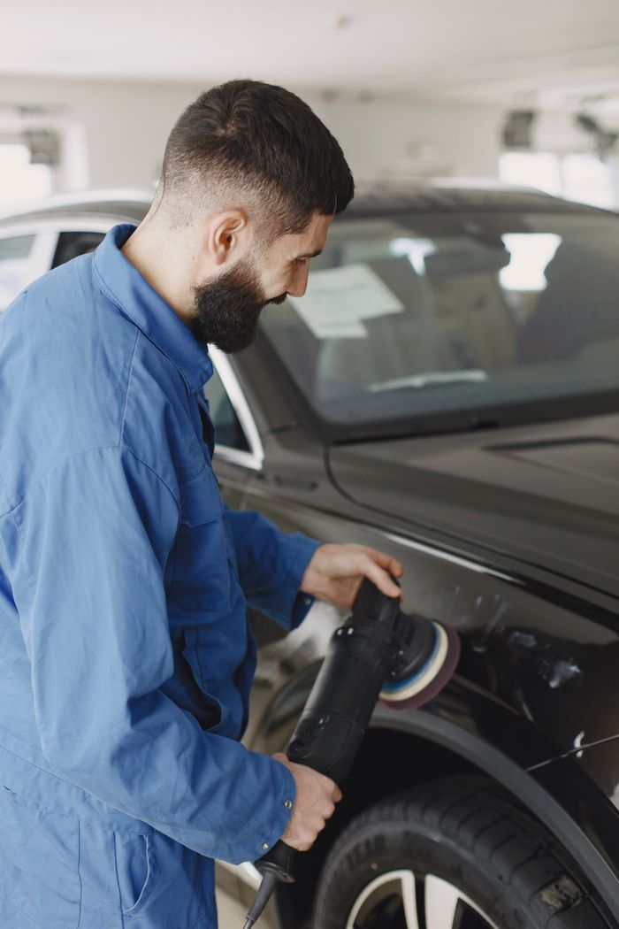 services-img Mechanic wearing blue uniform polishing car body with machine in workshop.