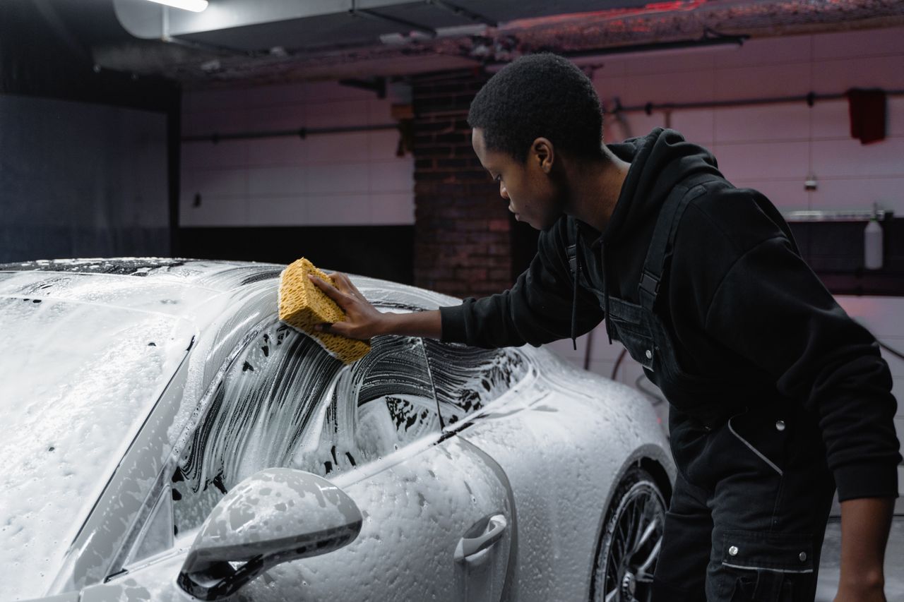 vision A young man cleans a luxury car with a sponge in an indoor carwash setting.