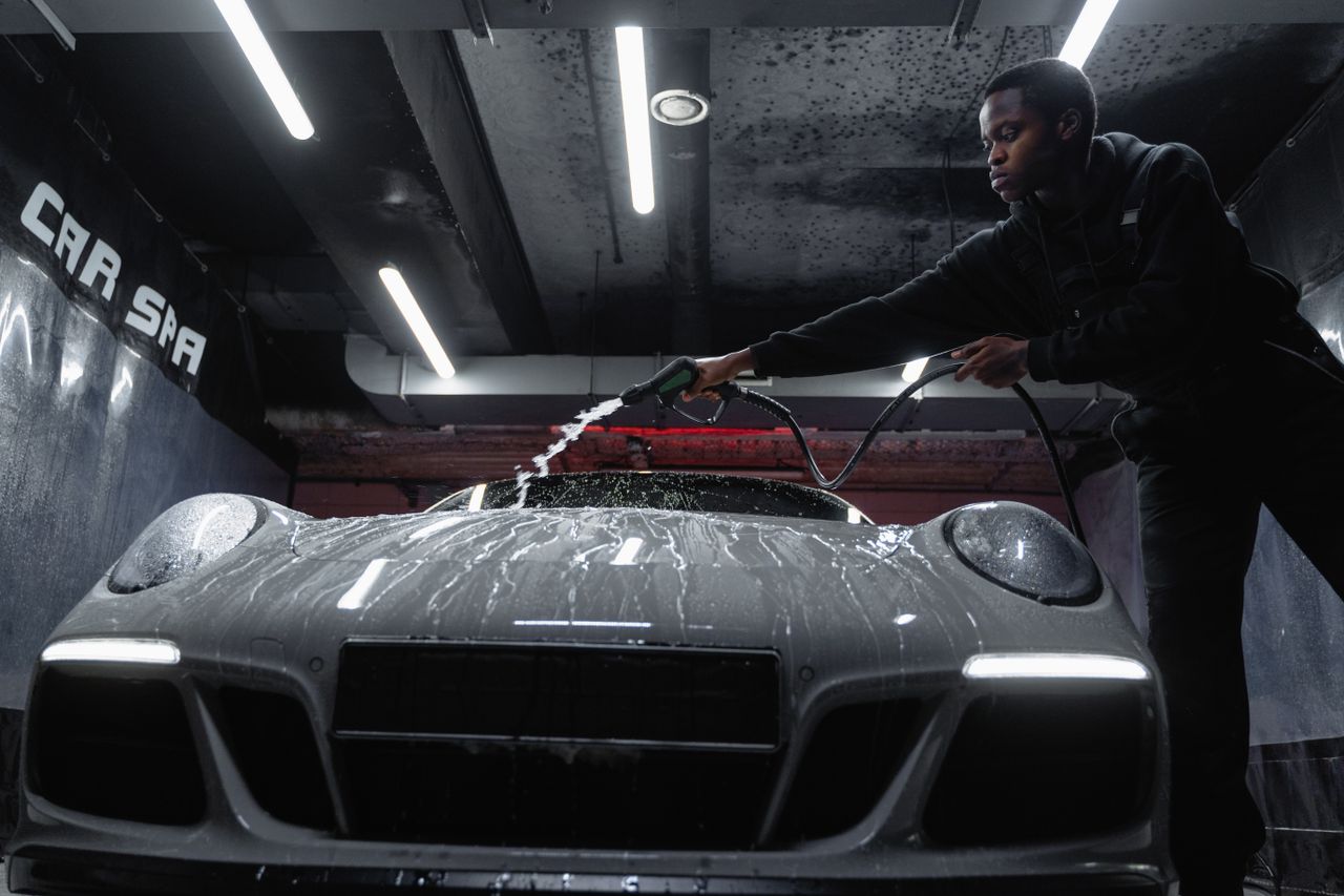 about-img African American man cleaning a white sports car at an indoor car wash. Low angle perspective.