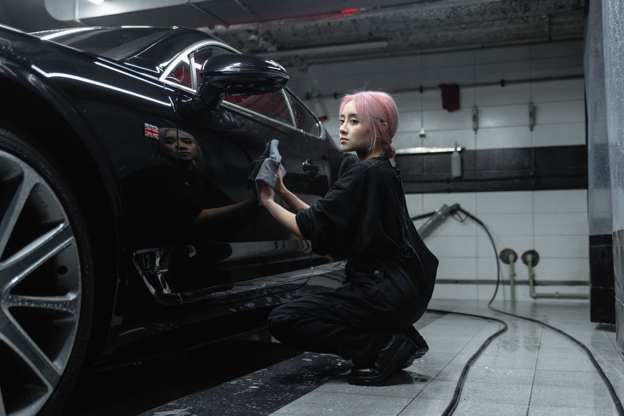 contact-img A young female worker polishing a black luxury car in an indoor garage setting.